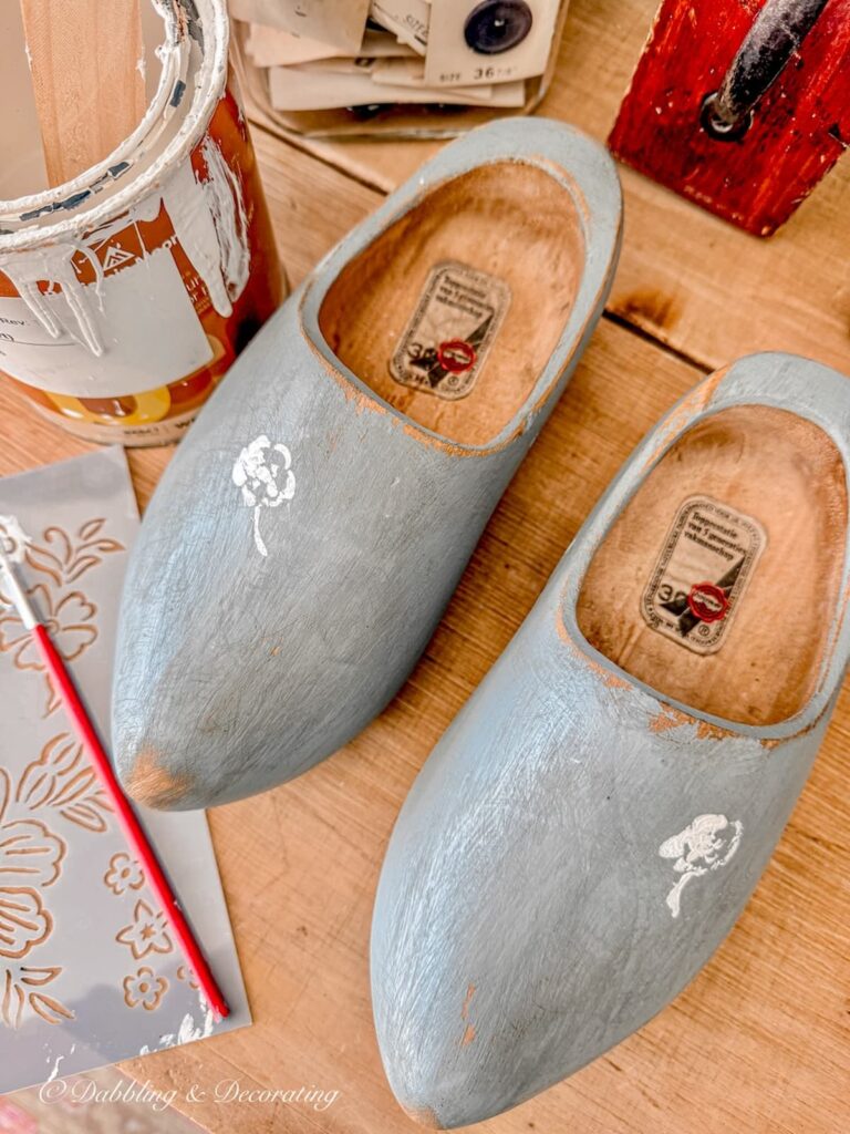 A pair of blue painted Dutch wooden clogs with stenciled white flower in the making.