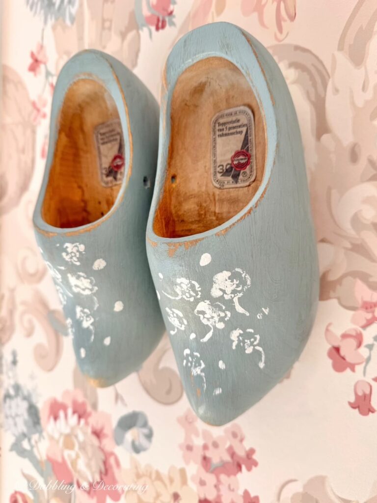 Blue wooden shoes hanging on pink wallpapered wall painted blue with white flower stenciling.