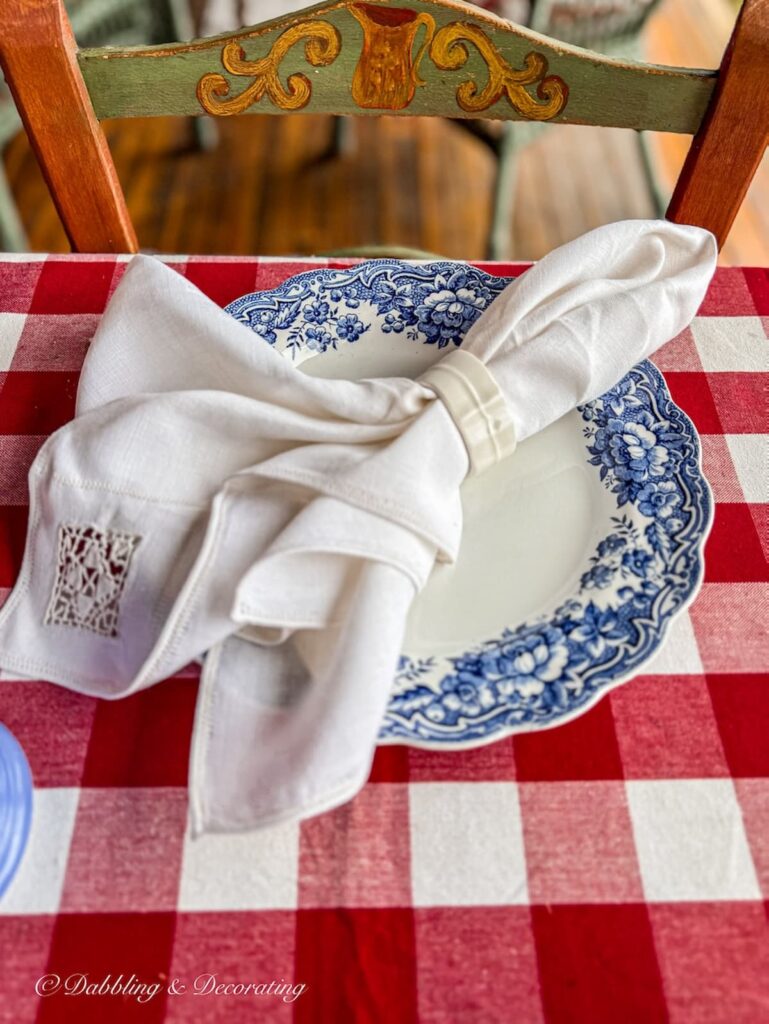 Red gingham tablecloth, vintage blue place setting with primitive chair as vintage home decor gifts.