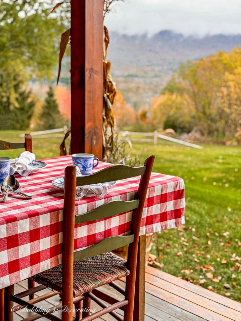 Vintage home decor gift ideas: A Pennsylvania Dutch vintage chair at outdoor table with red gingham tablecloth in the mountains during fall foliage.