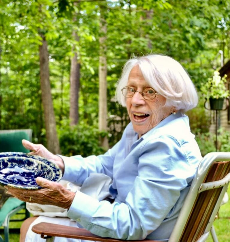 Smiling woman holding a vintage blue and white bowl outdoors — the joy of receiving a thrifted gift.