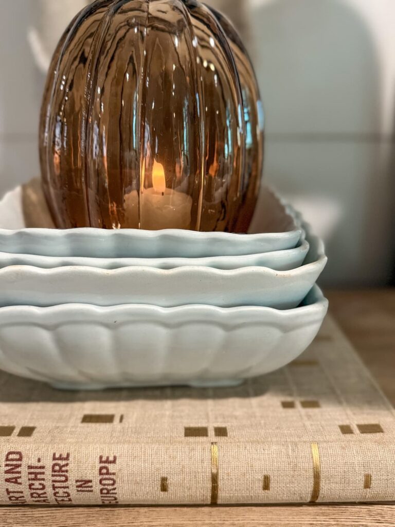 Amber glass pumpkin candle holder layered with vintage ironstone dishes.