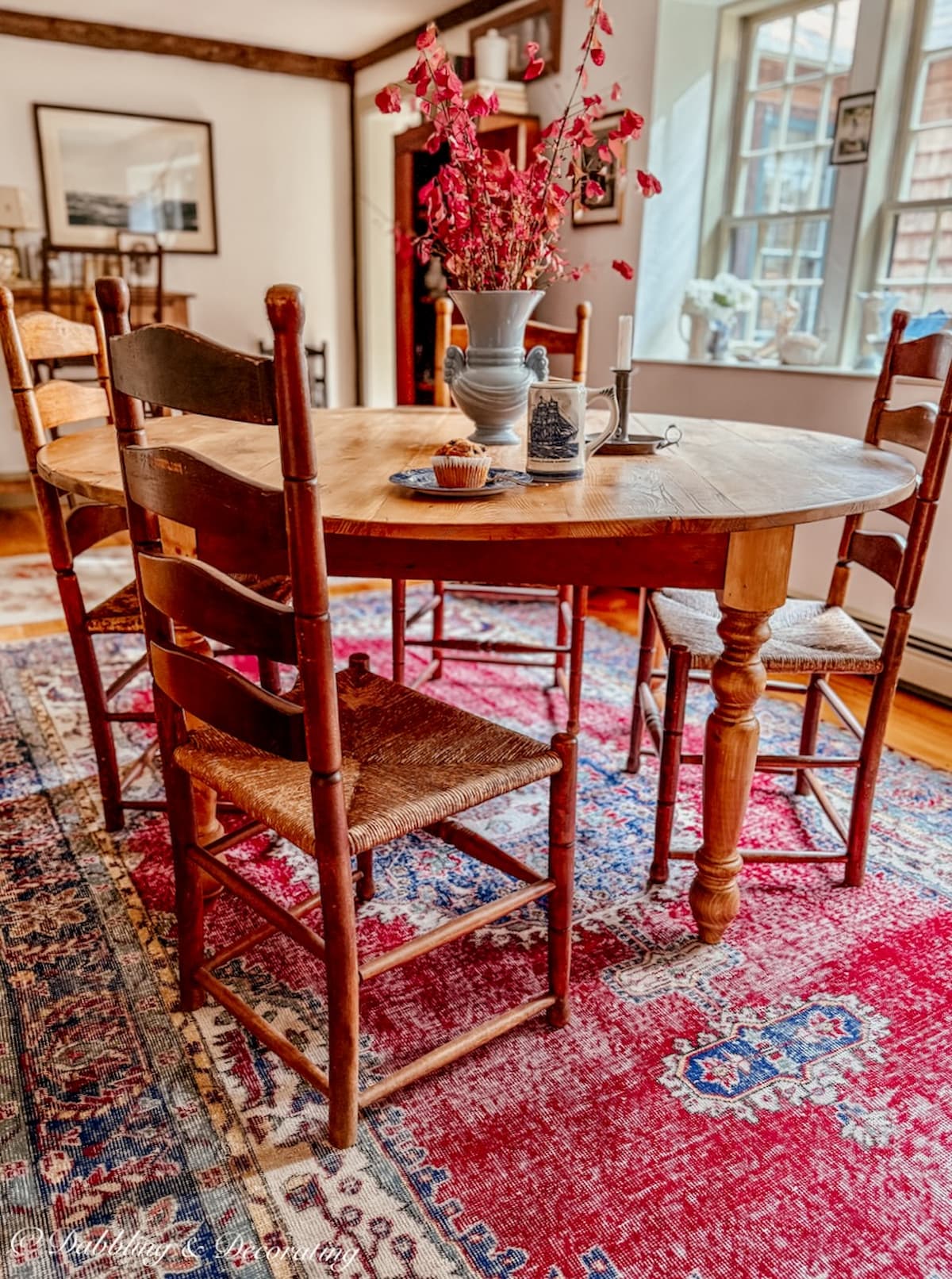 How to choose a vintage rug for a dining room with a round table and ladder back chairs in red with pine wood floors.