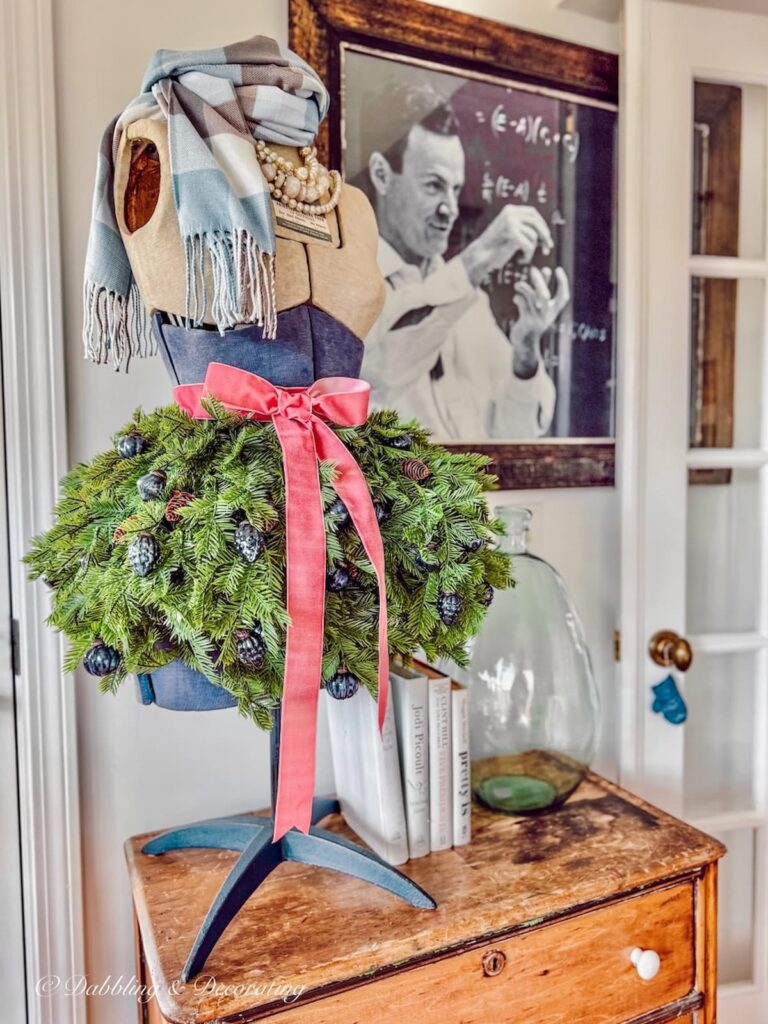 table top mannequin with faux evergreen dress, pink bow and blue and brown cashmere scarf on vintage dresser.