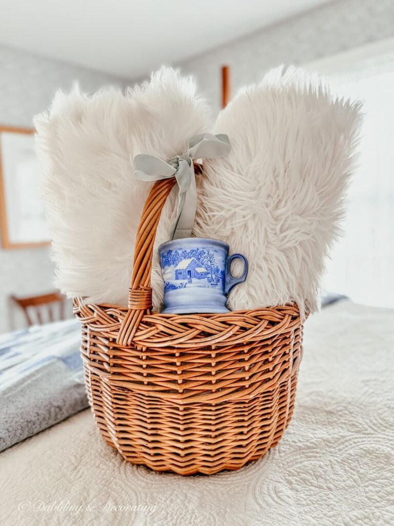 Basket with handle with sheepskins rolled up inside as a gift with a vintage blue coffee mug and blue bow as a present.
