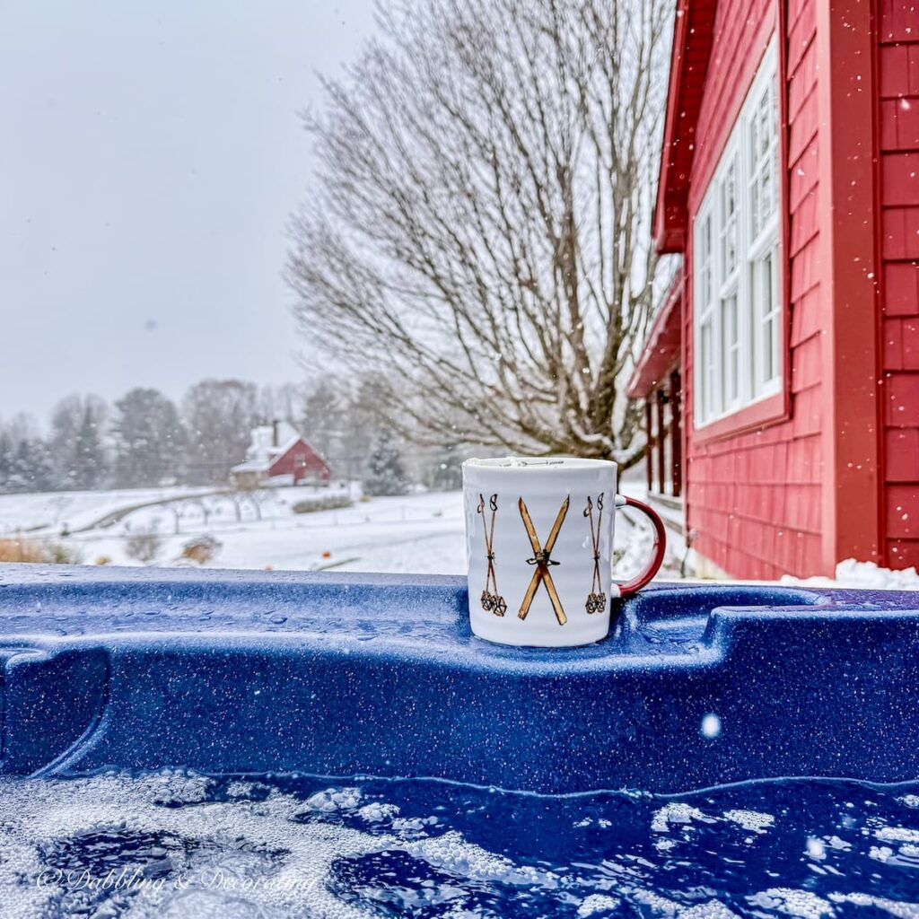 White Vintage style ski and poles mug on hot tub ledge and red house during an early November snowfall, winter decor style.