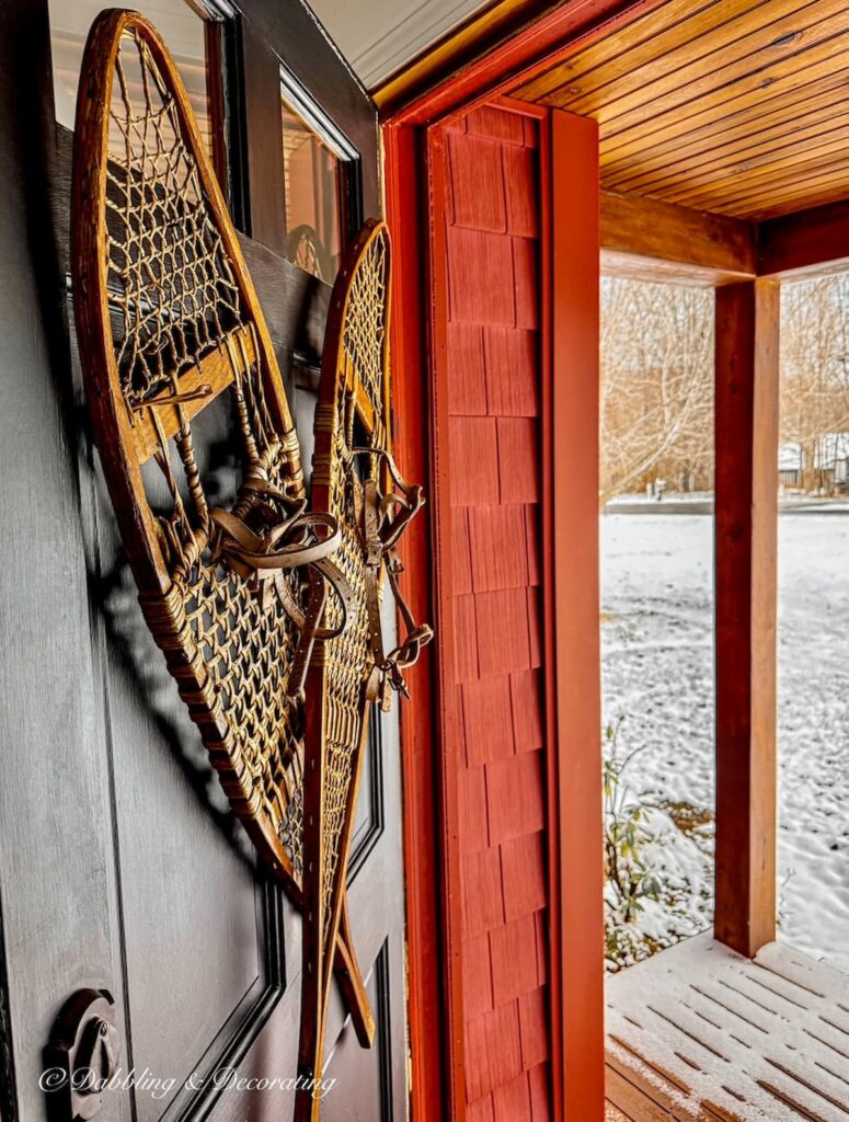 Antique wooden snowshoes on front door painted black on red house with snow in a winter decor style.