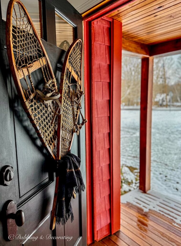 Wooden antique snowshoes criss crossed on black front door on red house for winter decor style.