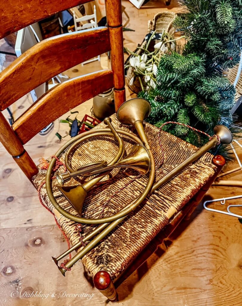 Collection of vintage brass horns on a ladder back antique chair in an attic hunting for vintage Christmas Decorations.