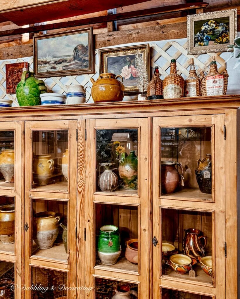 Antique pine cabinet with glass doors and pottery displayed at The Barn at Todd Farm in Rowley, Massachusetts.