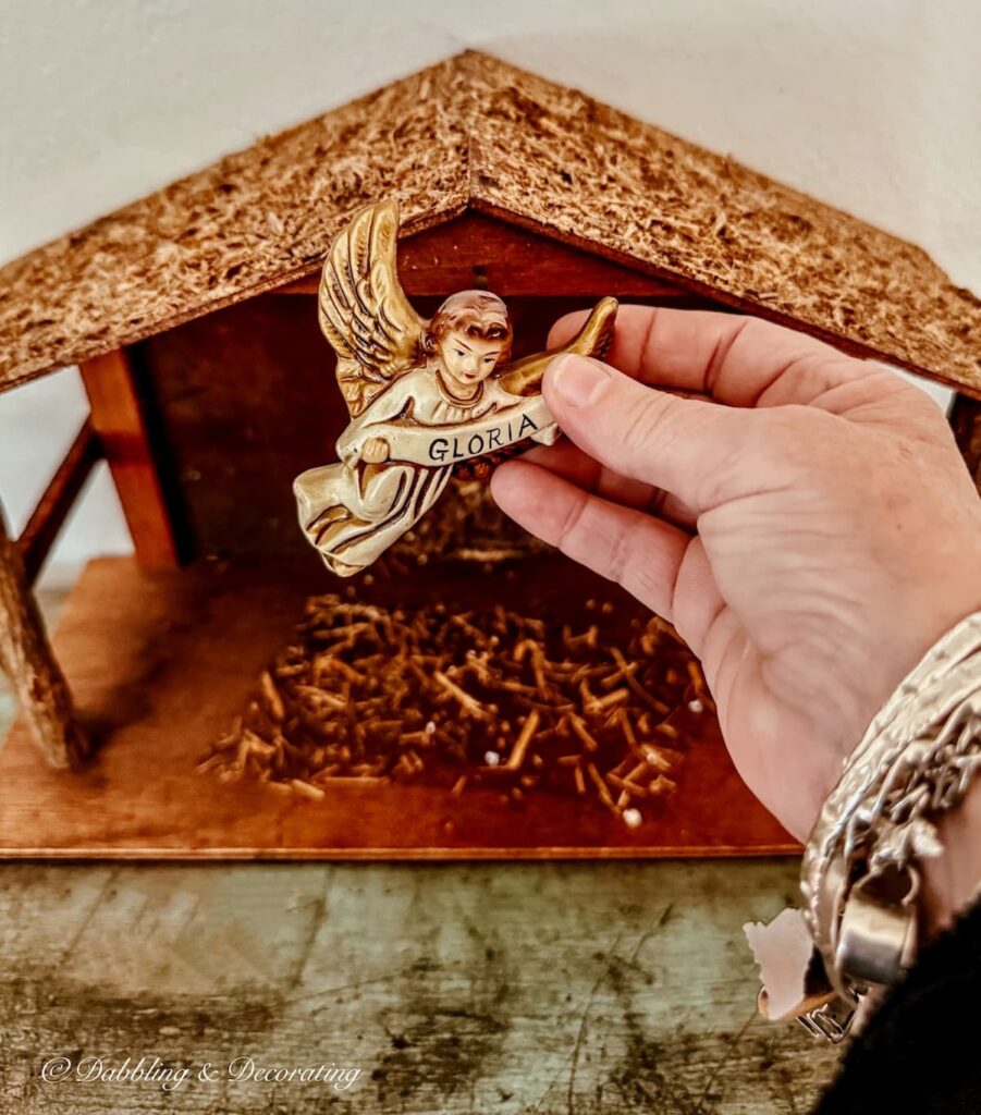 Vintage wooden Christmas manger with angel figurine that says Gloria in hand.