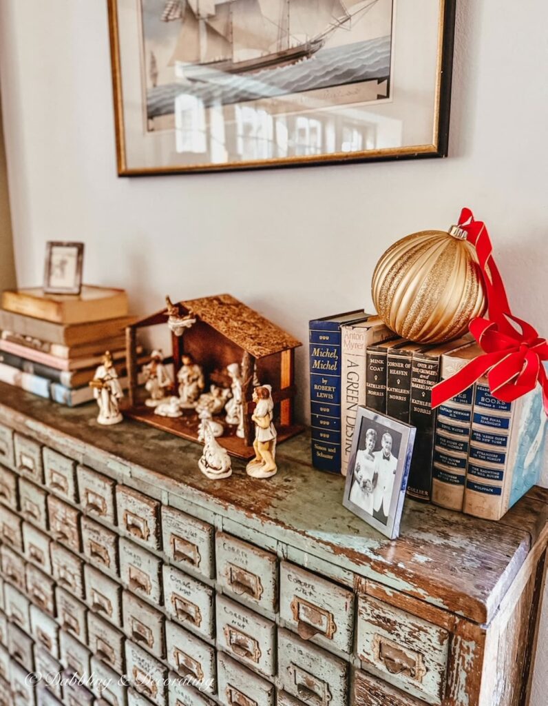 Antique apothecary with vintage Christmas decorations, a manger, and large gold Christmas ball on old books.