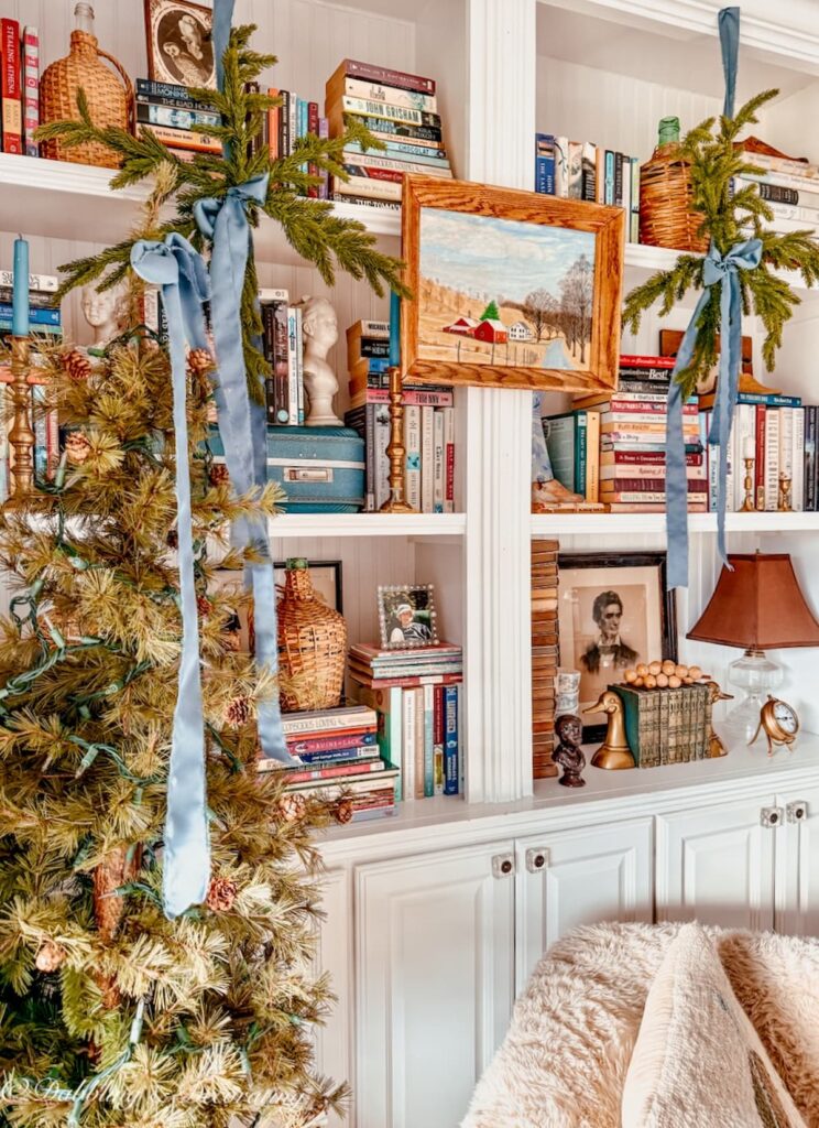 Christmas bookshelf decor with evergreens and blue ribbon, vintage details, and woodland inspired.