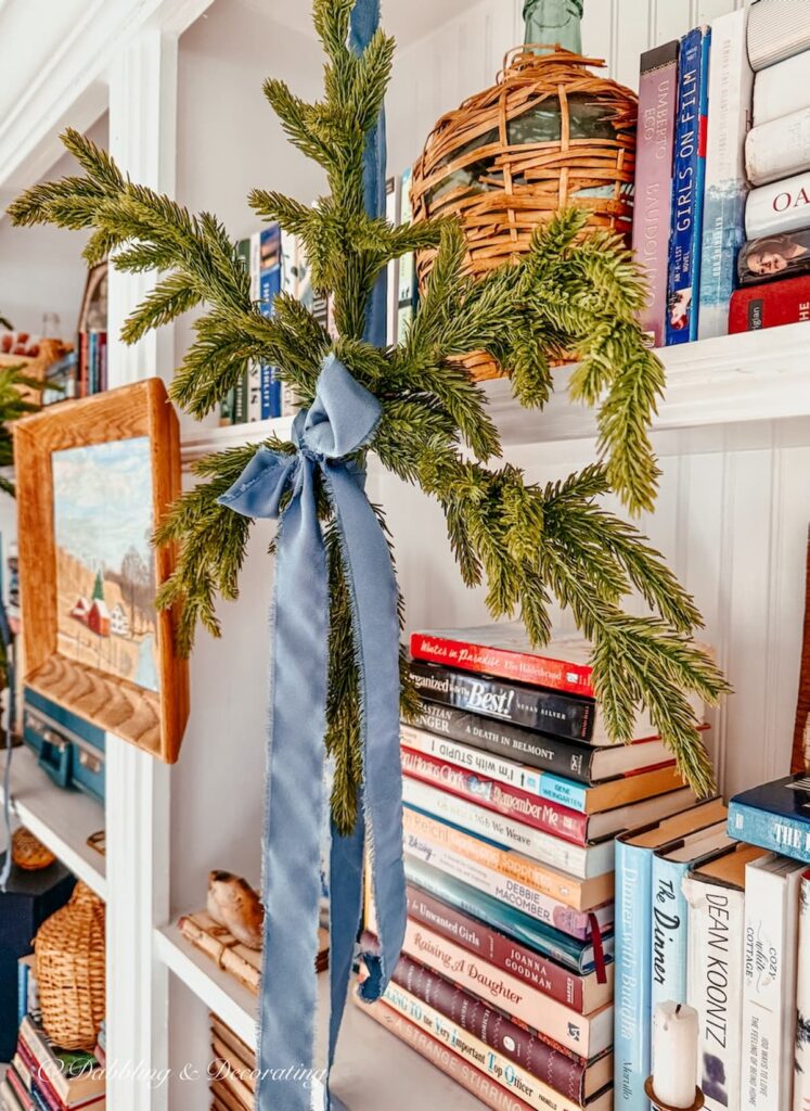 Christmas Bookshelf decor with eclectic style using Anthropologie faux evergreen snowflakes and satin blue ribbon with vintage style.