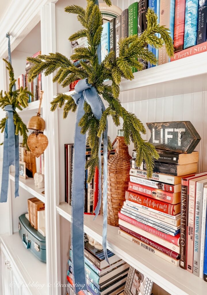 Christmas Bookshelf decor with eclectic style using Anthropologie faux evergreen snowflakes and satin blue ribbon with vintage style.