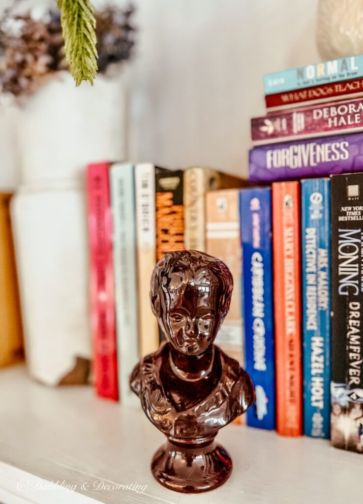 Vintage brown small porcelain bust on bookshelf with stacked books.