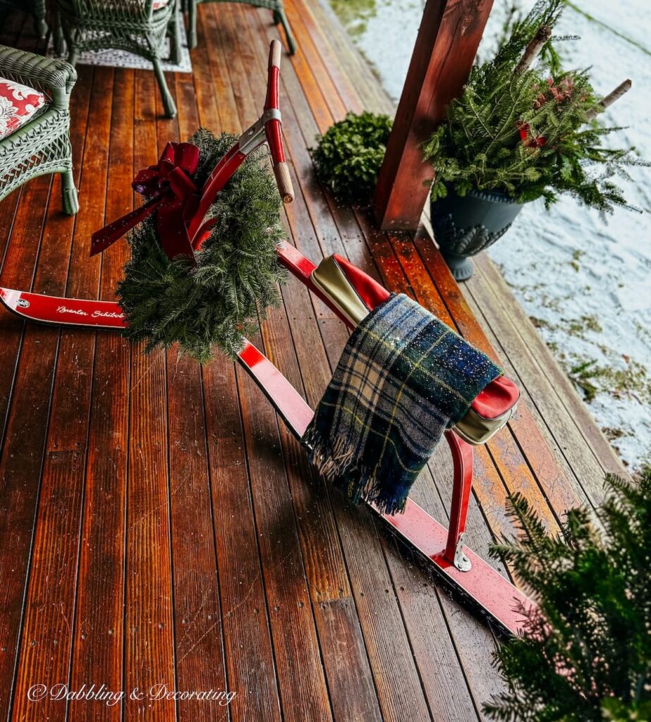 Vintage ski bob from French Alps with plaid blanket and wreath with burgundy bow in Christmas Après ski porch decor.