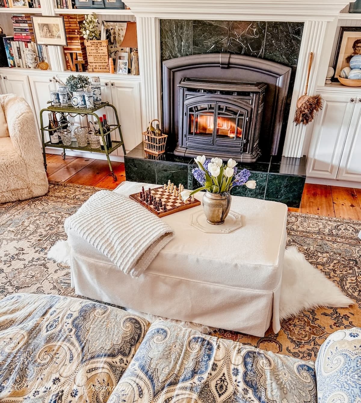 Cozy living room with black pellet stove going and white ottoman layered on brown vintage rug with white sheepskin decor ideas in cozy living room