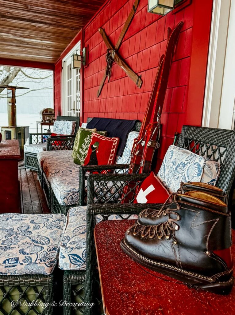 Après Ski Christmas Porch Decor with vintage ski lodge decor like ski boots, skis and cozy pillows on outdoor wicker furniture.