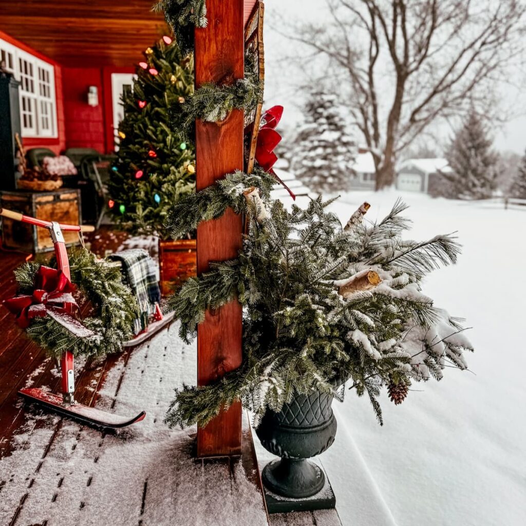 Après Ski Christmas Porch Decor with urns on steps filled with evergreens and birch logs, Christmas tree and vintage French Ski Bob on a snowy Vermont day.