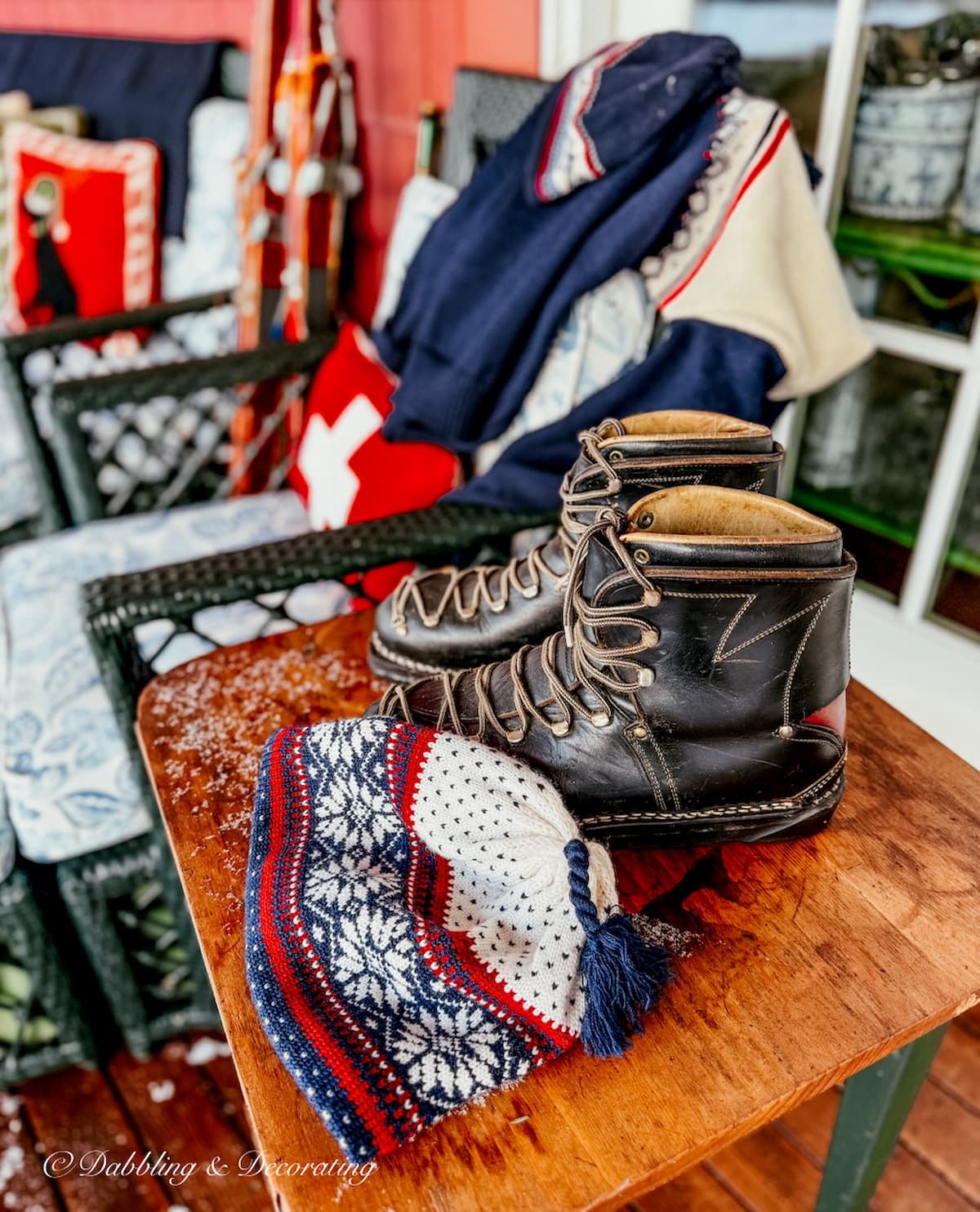 Vintage ski hat, ski boots, ski sweater draped on side table and outdoor porch chair in Après Ski Christmas Porch Decor.