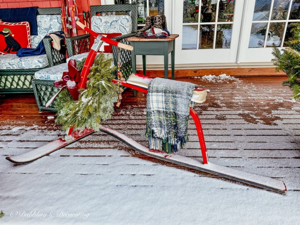 Vintage French Alps ski bob in Après Ski Christmas Porch decor in the snow with wreath and plaid blanket.