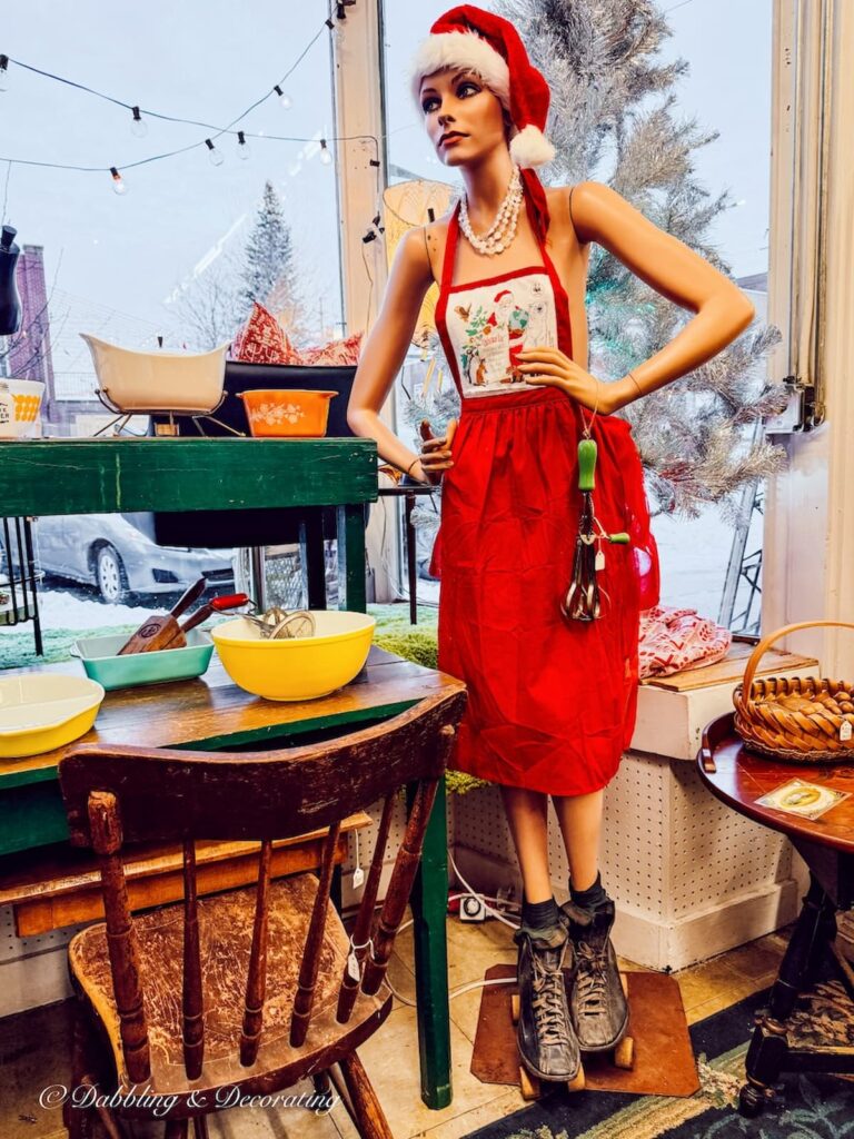 Life like female mannequin with a red apron, antique roller skates and kitchen utensil inside Across the Street Antique shop in Brandon, Vermont.