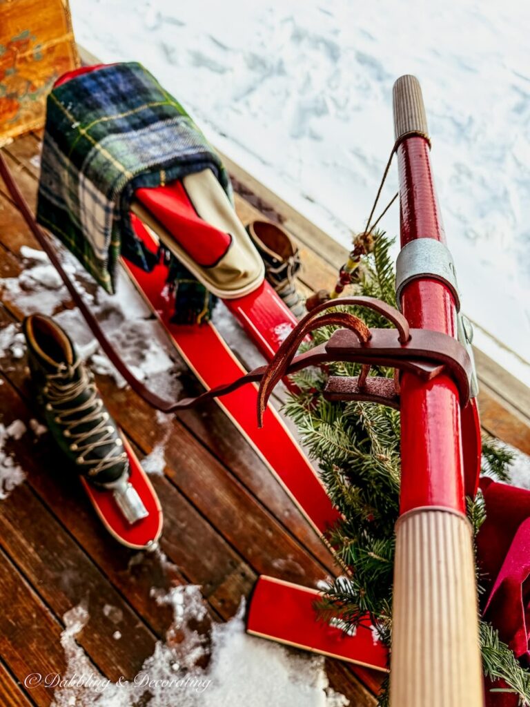 Close up of vintage French ski bob on Après ski porch with leather reins tied to handle and vintage ski boots on the ground.
