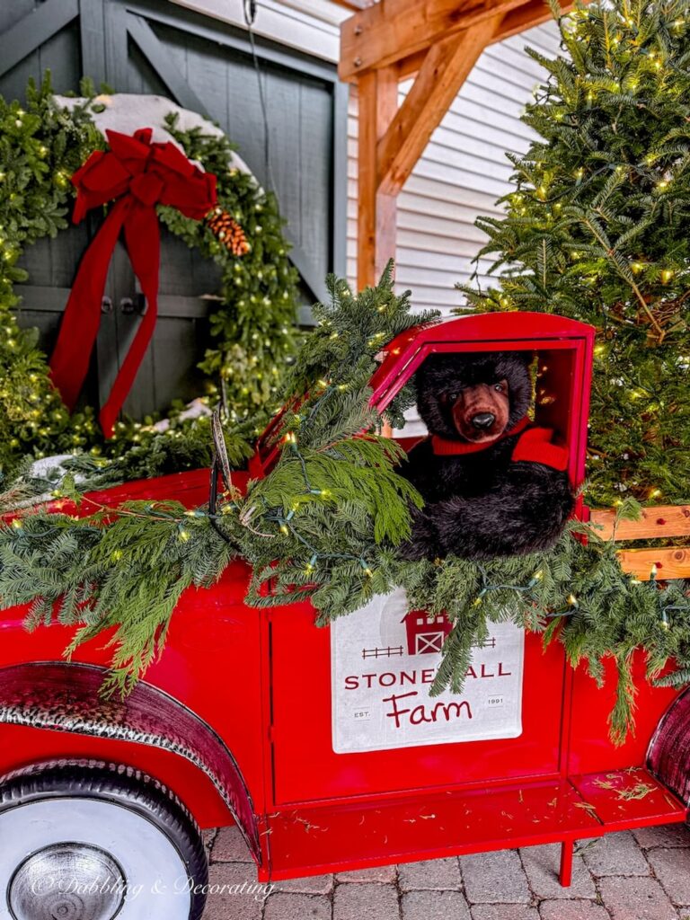 Stonewall Kitchen's iconic red truck and Maine bear driving covered in evergreens display at front door for the holidays.