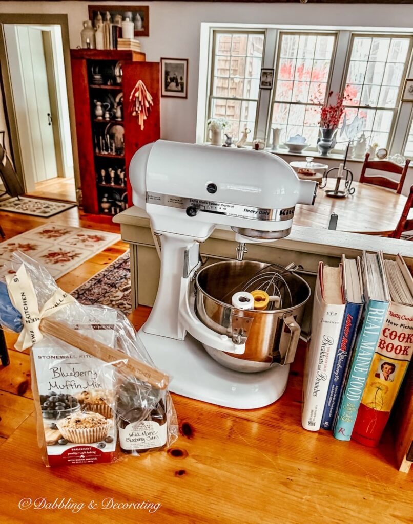 Large white KitchenAid with Stonewall Kitchen's blueberry muffin gift bag and vintage cookbooks on country style kitchen wood counter in winter home decor.