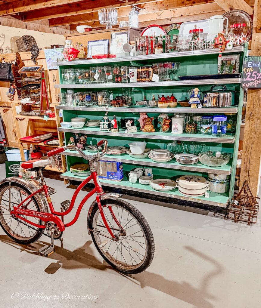 Inside a charming vintage vendor booth at the Willows flea market, Maine's largest indoor flea market. Red bicycle and green shelves filled with antique smalls.