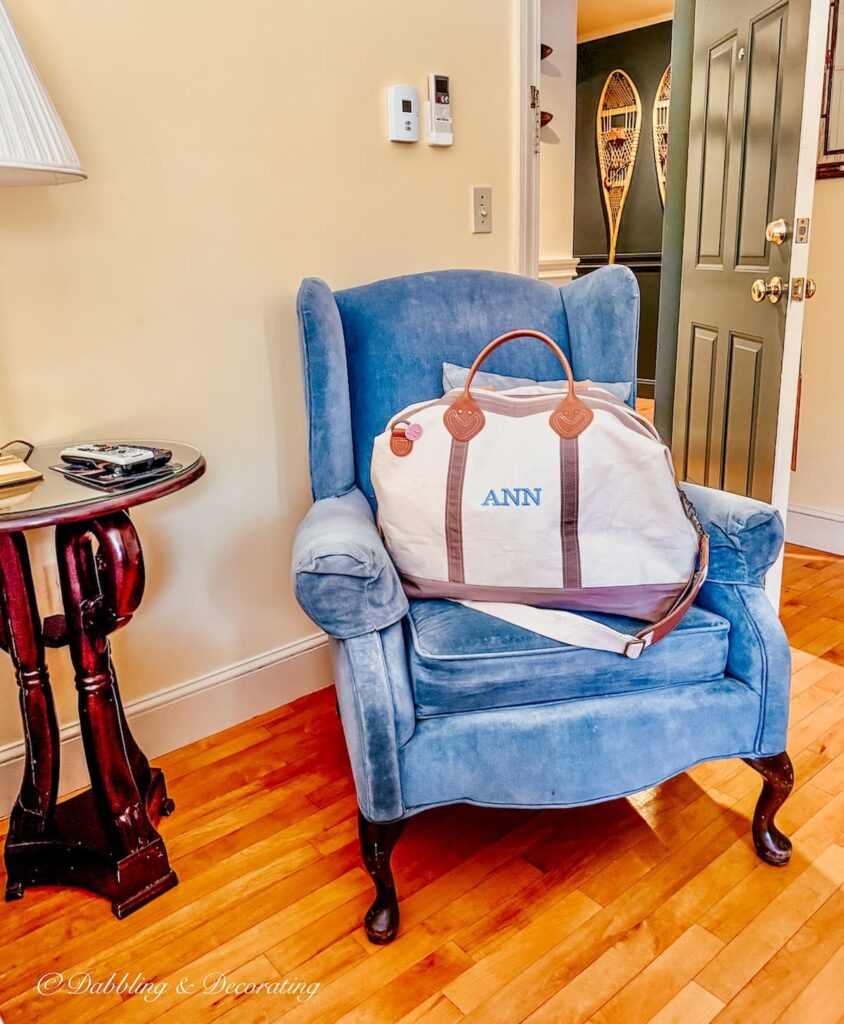 Blue velvet chair with canvas overnight bag in guest room at the Wolf Cove Inn in Poland, Maine.