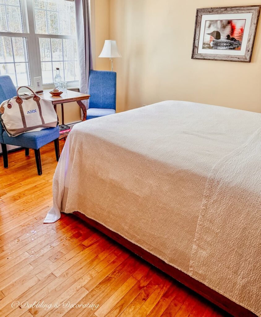 Guest bedroom with bed and two blue chairs with a canvas bag at the Wolf Cove Inn in Poland, Maine.