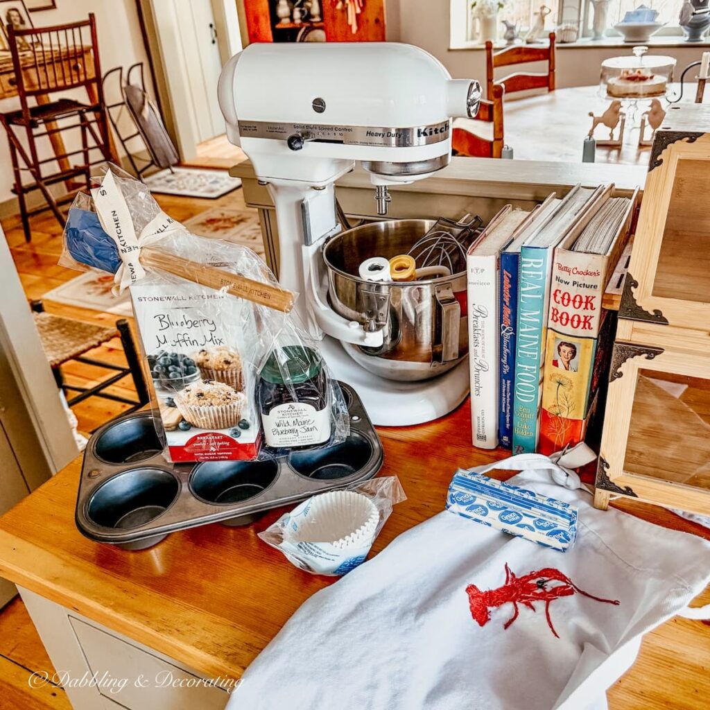 Thrifted Goodwill Northern New England KitchenAid Mixer on wooden counter tops with blueberry muffin mix, cupcake tin, apron and vintage cookbooks in kitchen for winter home decor ideas.