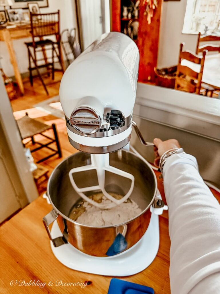 Thrifted white KitchenAid Mixer and hand leveling the bowl while making blueberry muffins on a cozy winter day in Maine.