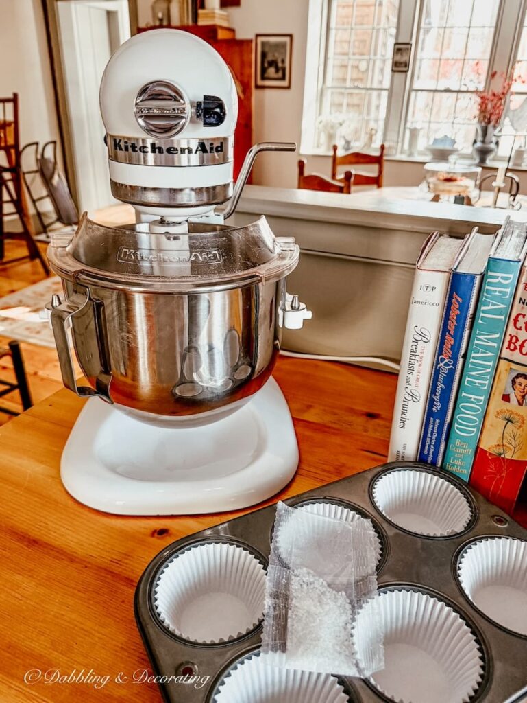 White KitchenAid Mixer on wooden kitchen counter tops with vintage thrifted cupcake tin and vintage books in cozy winter home decor.