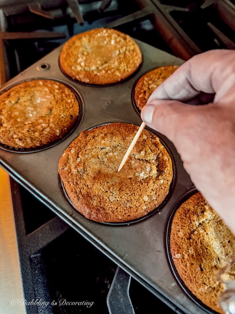 Person testing blueberry muffins in the oven with a toothpick.