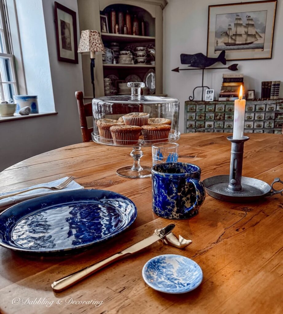 Cozy thrifted winter home decor ideas with a breakfast place setting, a cake stand filled with blueberry muffins made from a Goodwill KitchenAid Mixer.