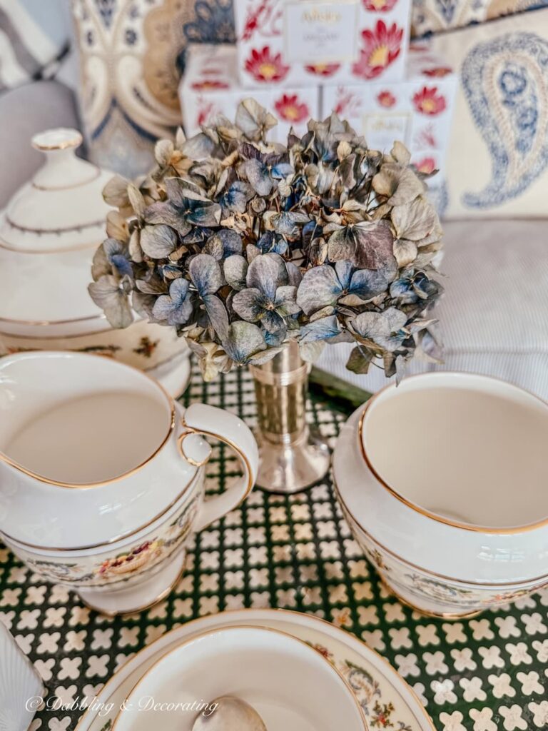 Small silver bud vase with one blue stem dried hydrangea on tea cart with Anysley's Banquet tea set.