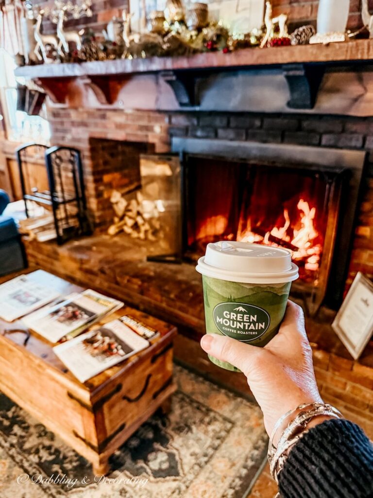 Vermont Green Mountain coffee to go in hand in front of fireplace at the Quechee Inn at Marshland Farm.