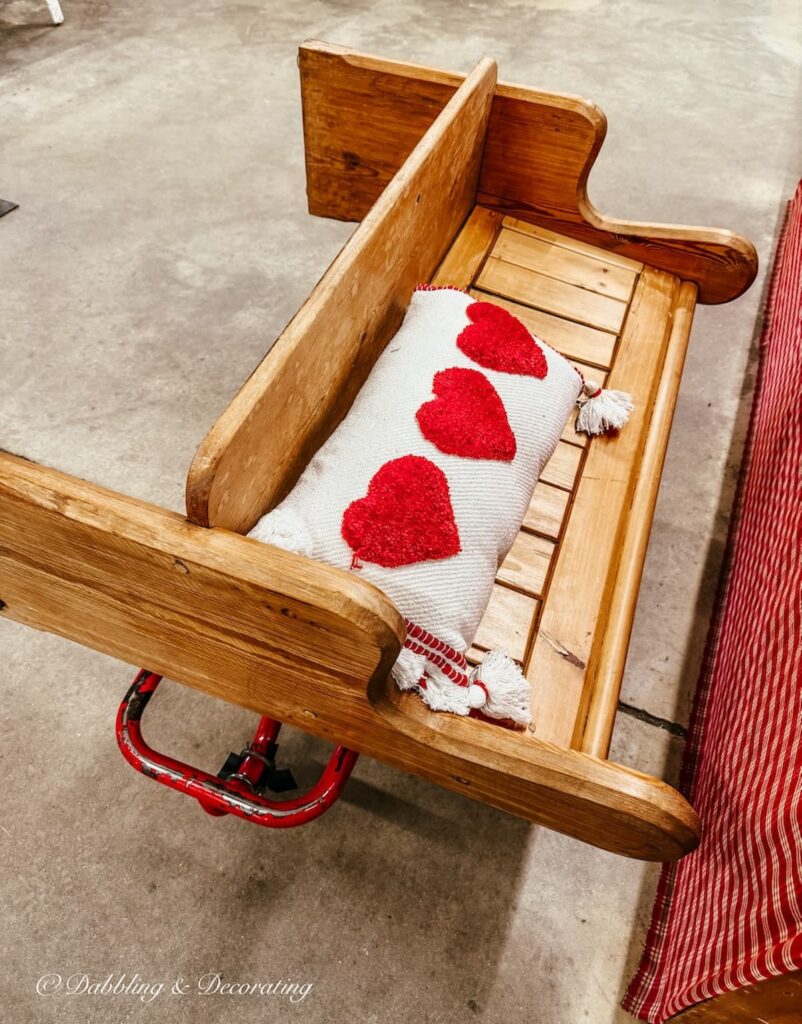 Vintage church pew bench at antique store on rolling cart with red heart pillow for entryway.