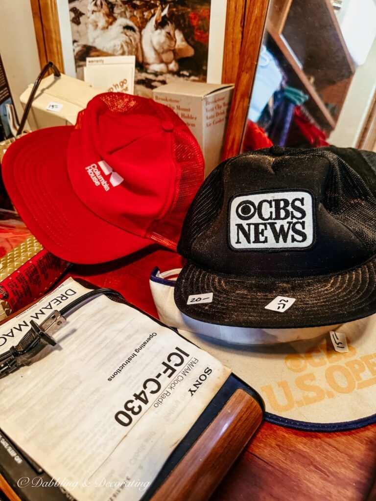 Two baseball hats from CBS News and Columbia Records Studio in closet at estate sale.