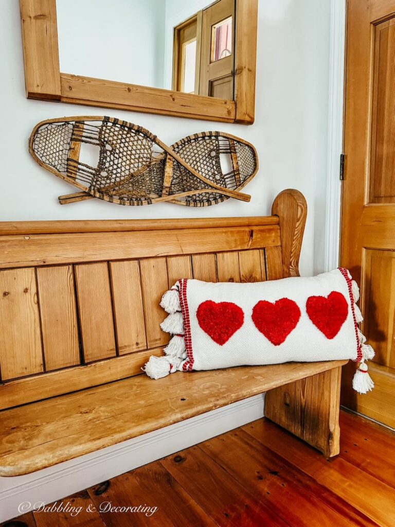 Church pew bench entryway with Valentine's Day pillow, snow shoes and pine mirror on wall.