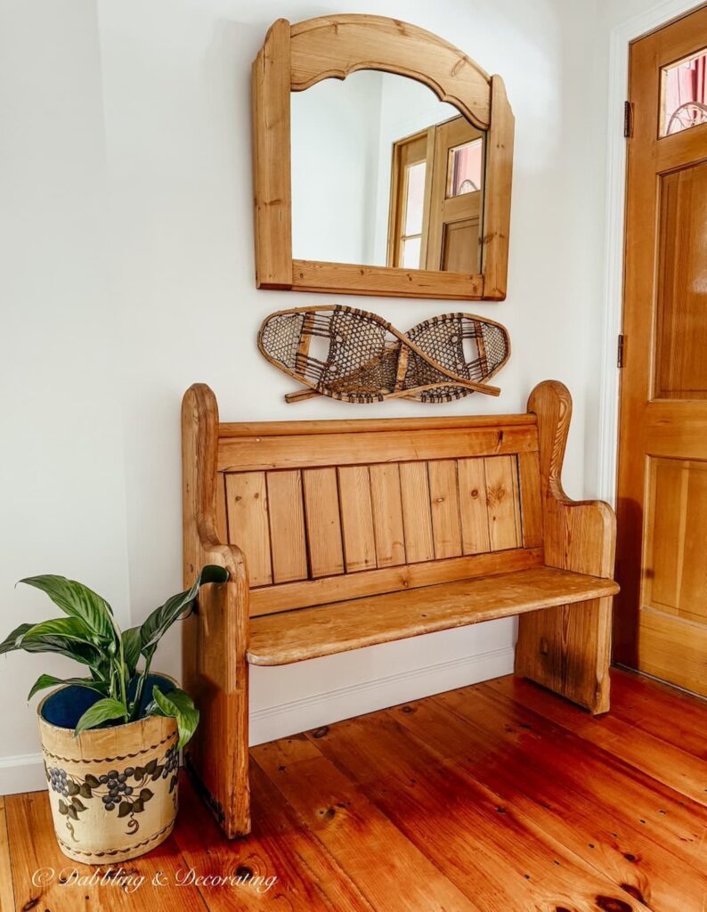 Church pew bench entryway with overhead mirror and criss crossed snow shoes on wall and a blueberry bucket with greenery.