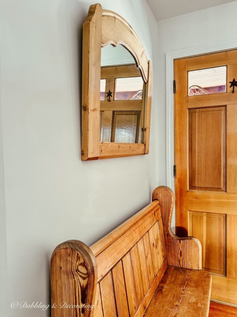 Small home's entryway with vintage pine wood church pew with hanging pine mirror above it on the wall.