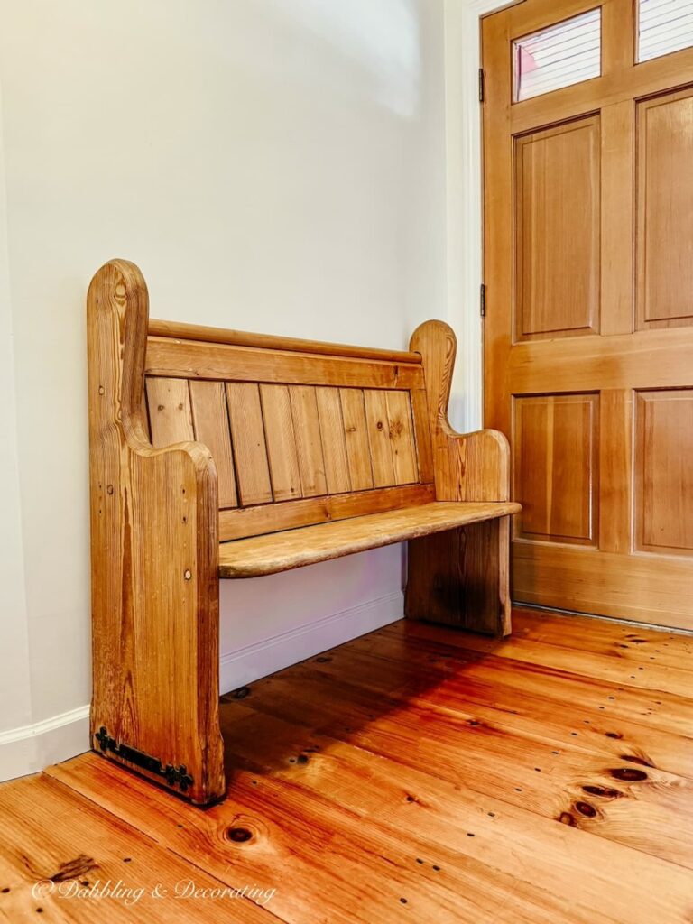 Vintage pine wood church pew in small entryway with pine flooring and door.