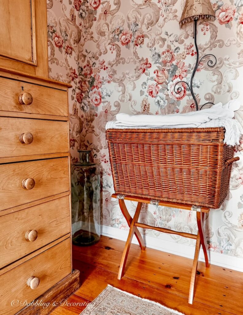Vintage wooden luggage rack with large basket on it in bedroom next to pine dresser found at a luxury estate sale.