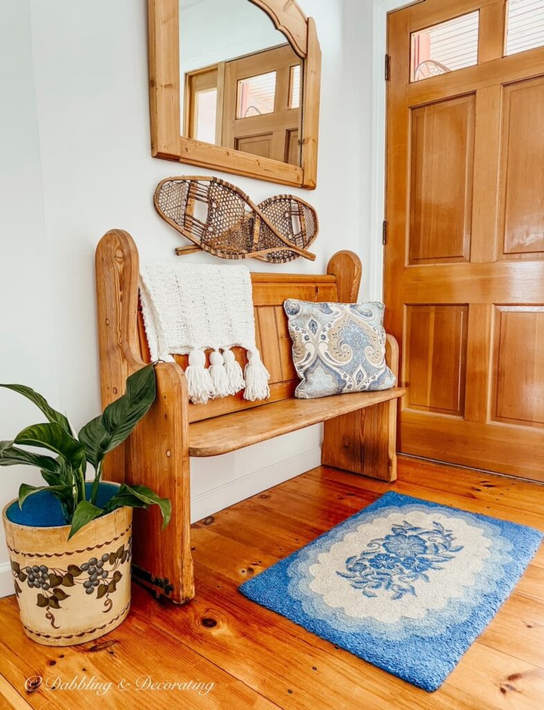 Vintage church pew bench entryway decorated with a blue throw rug, paisley blue pillow and white throw.
