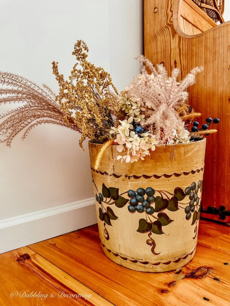 Antique blueberry bucket filled with dried fall foraged weeds next to church pew bench entryway.