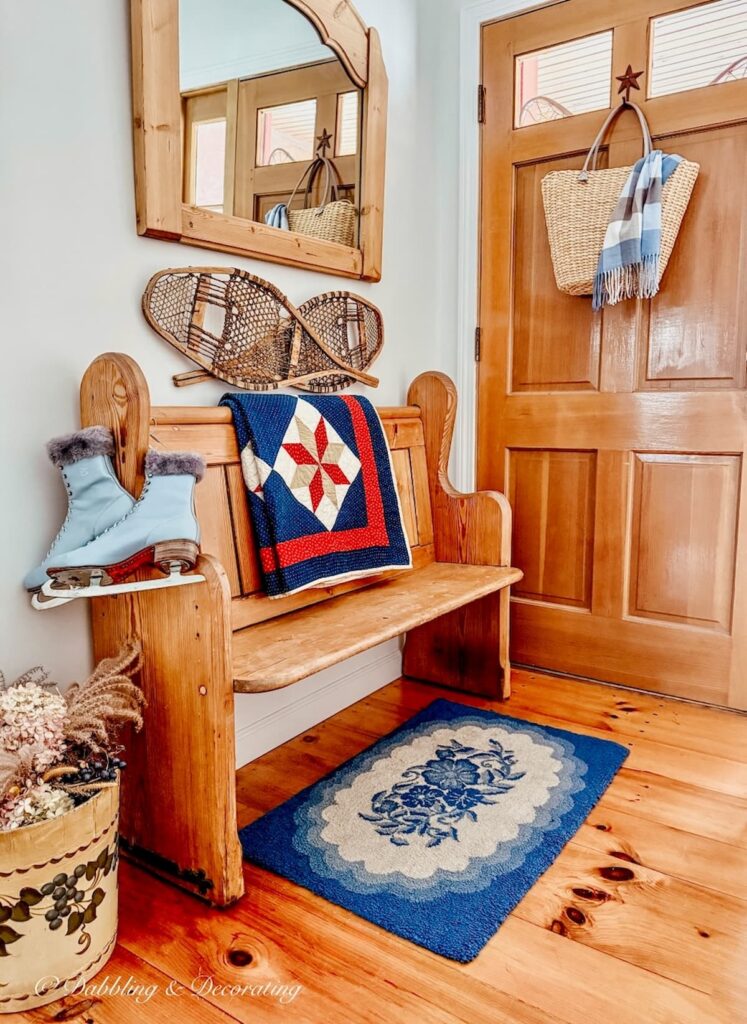 Vintage church pew bench entryway decorated with winter decor like blue ice skates quilt, and snowshoes with a blue rug on floor.